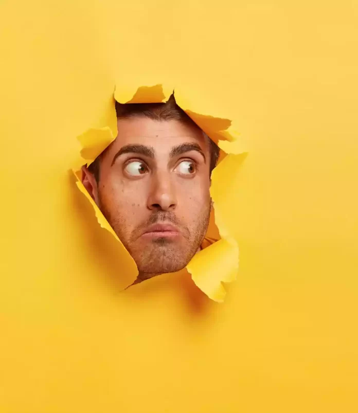 cara-joven-asustado-sorprendido-mira-lado-traves-agujero-papel-amarillo-ve-algo-impactante-tiene-ojos-bien-abiertos